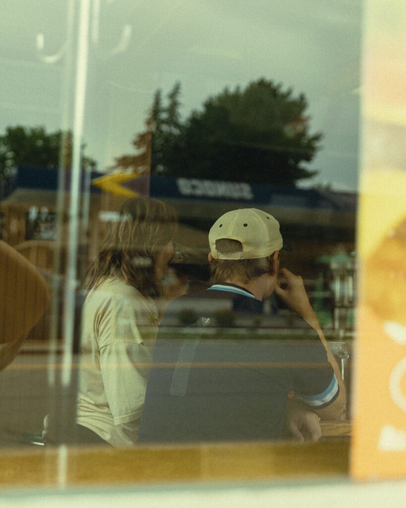 a couple on the other side of a window sit together at a bar during their couples photography