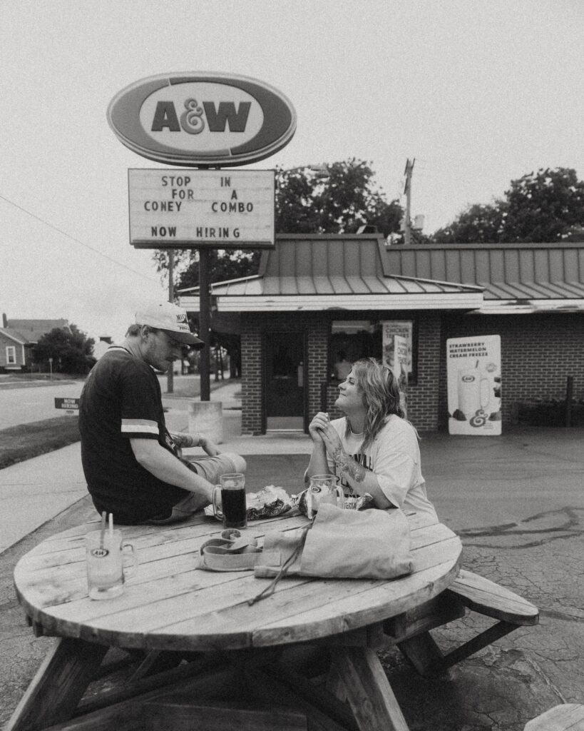 a couple eat together at an outdoor wooded picnic table outside of an a&w during their couples photography