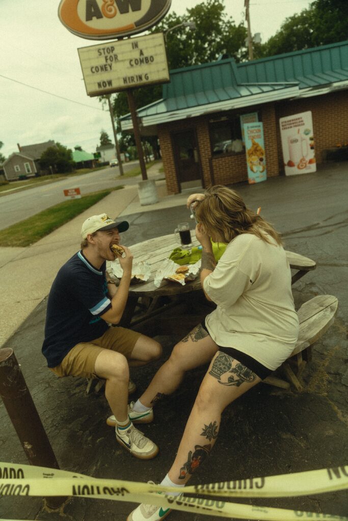 a couple shares a meal on an outdoor picnic table in front of an a&w