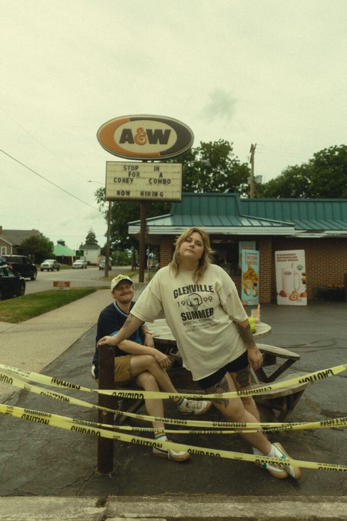 a woman leans against a pole in front of a fast food restaurant as her partner smiles at her from behind her