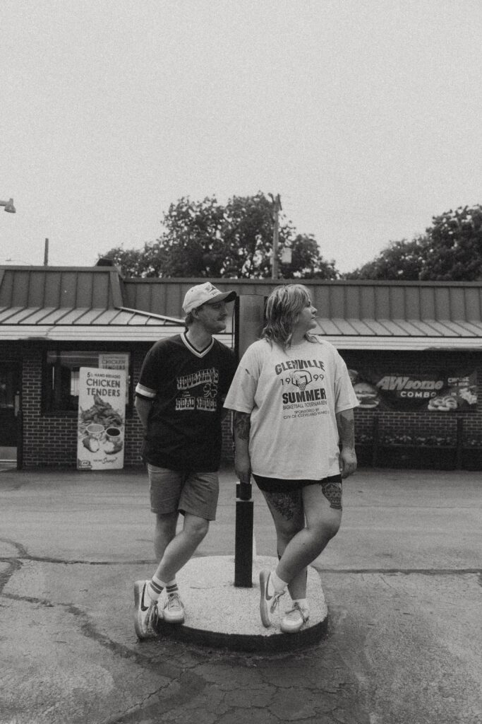 a black and white portrait of a couple looking to their lefts in the fast food parking lot during their couples photography