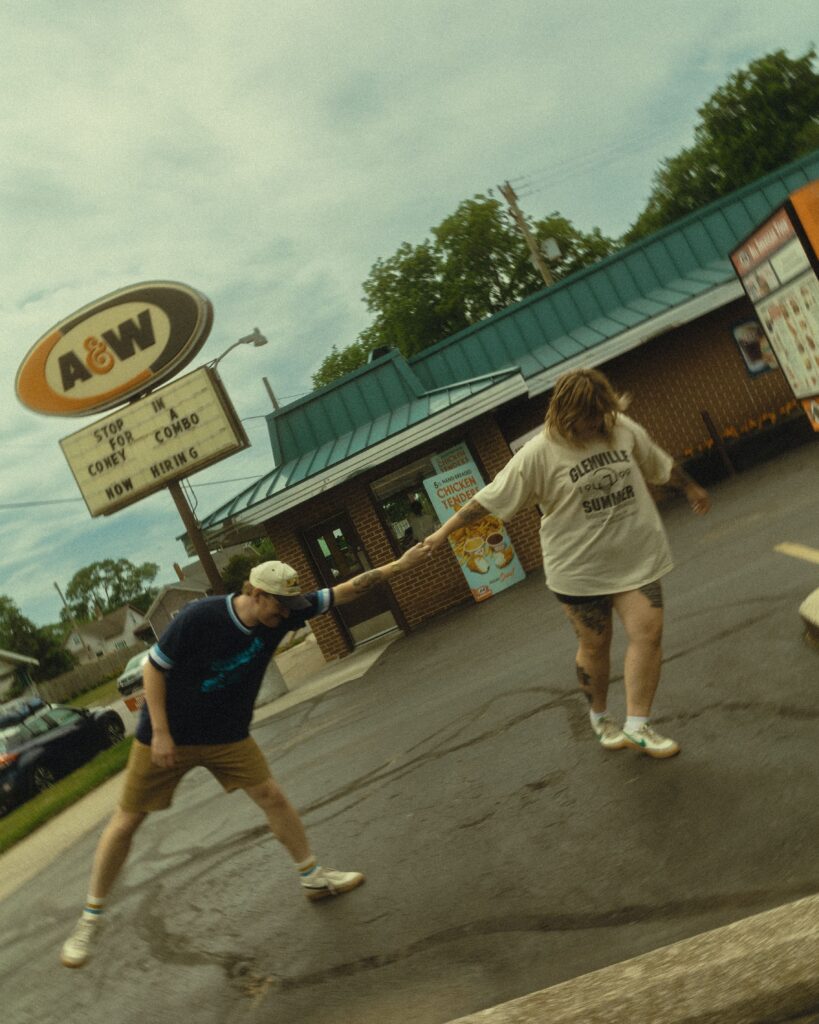 a couple pull on each others arms as they stand in front of a fast food stop during their couples photography