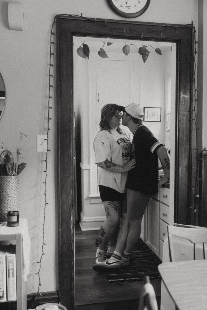 a couple stand together in the kitchen doorway leaning in for a kiss