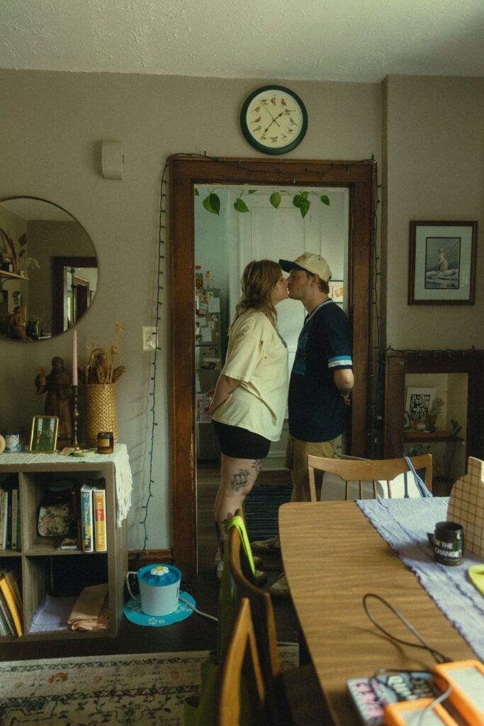 a couple share a kiss in the doorway of their kitchen