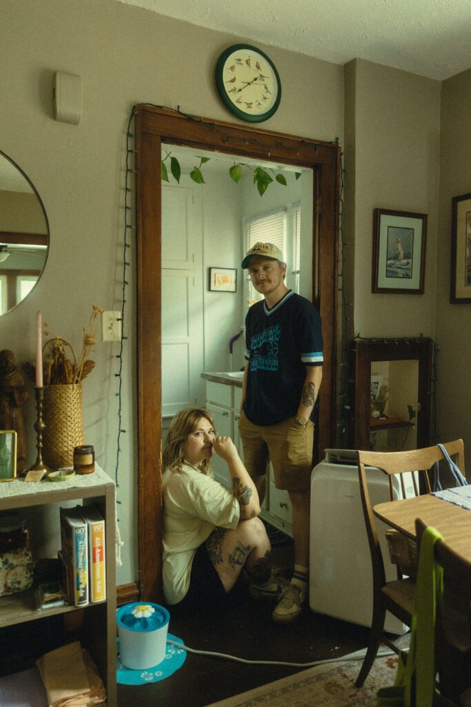 during their couples photography, a woman sits against the kitchen doorway as her partner stands next to her