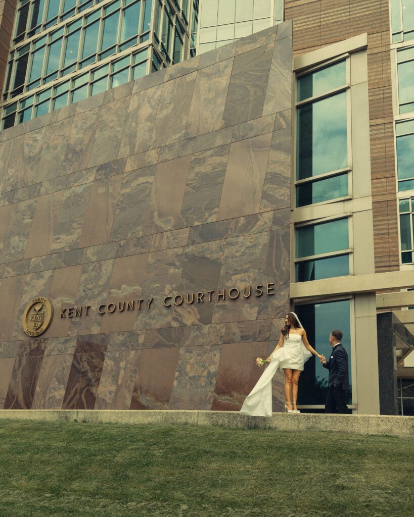 a couple stands together in front of the kent count courthouse while eloping in michigan