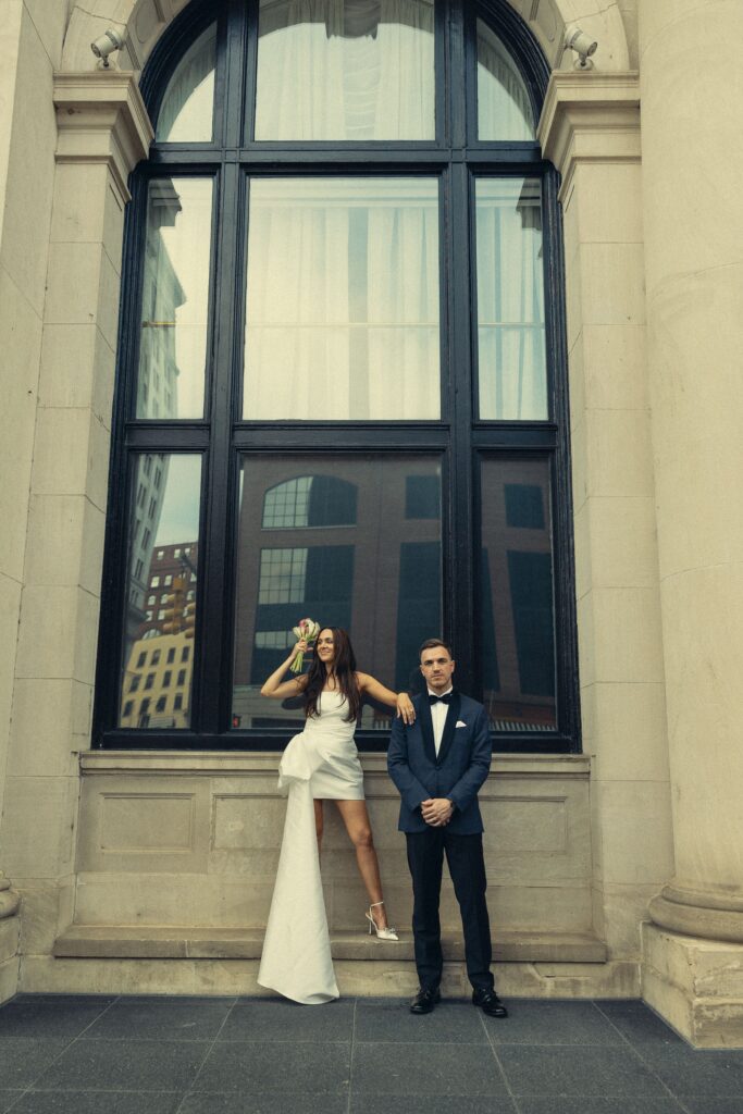 a couple in wedding attire stand in front of an arched window during their elopement, how to elope in michigan