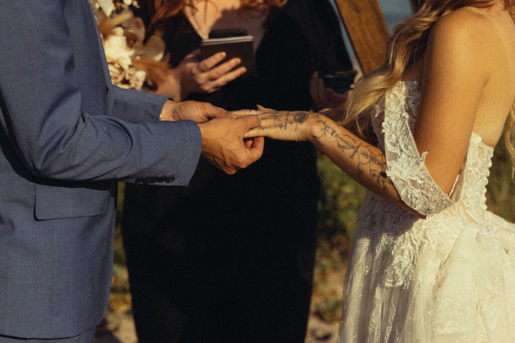 a man slides a ring on to a woman's finger at a beach