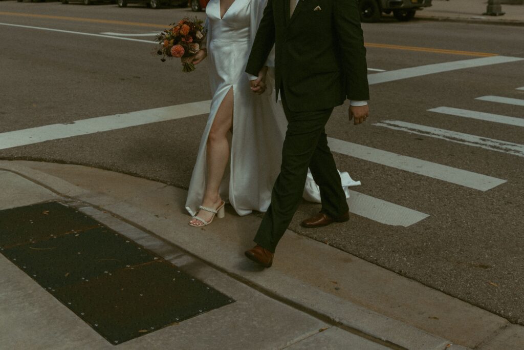 how to elope in michigan, a couple wearing wedding outfits cross a crosswalk