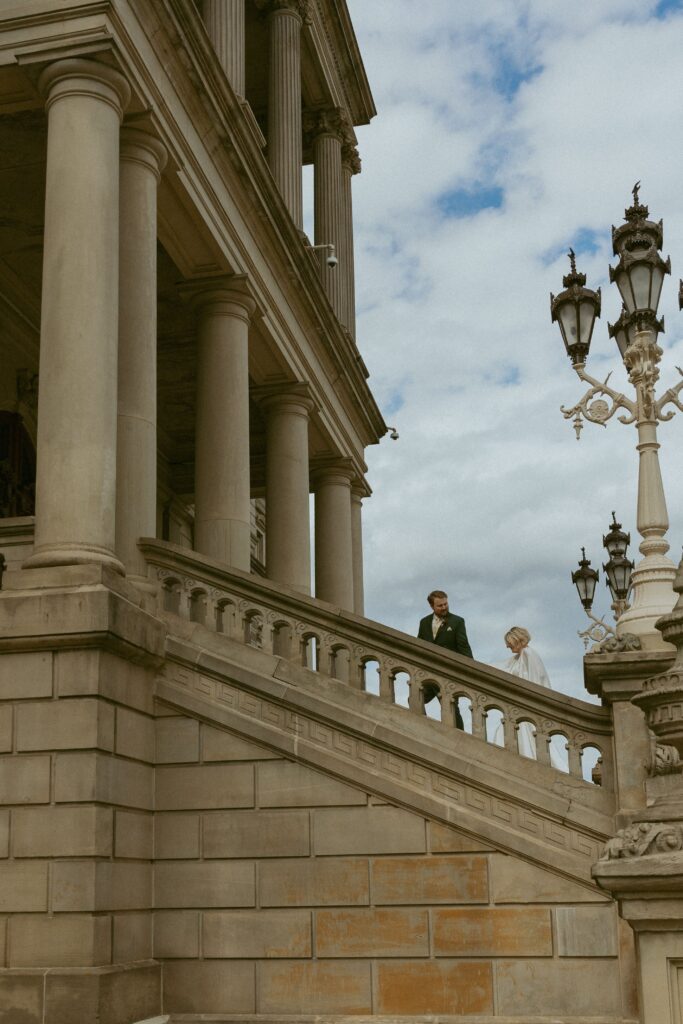 how to elope in michigan, a couple in wedding attire climb the stairs of a massive stone building