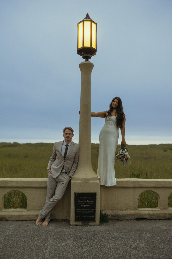 a woman swings from a lamppost as her husband leans against the other side for elopement photography