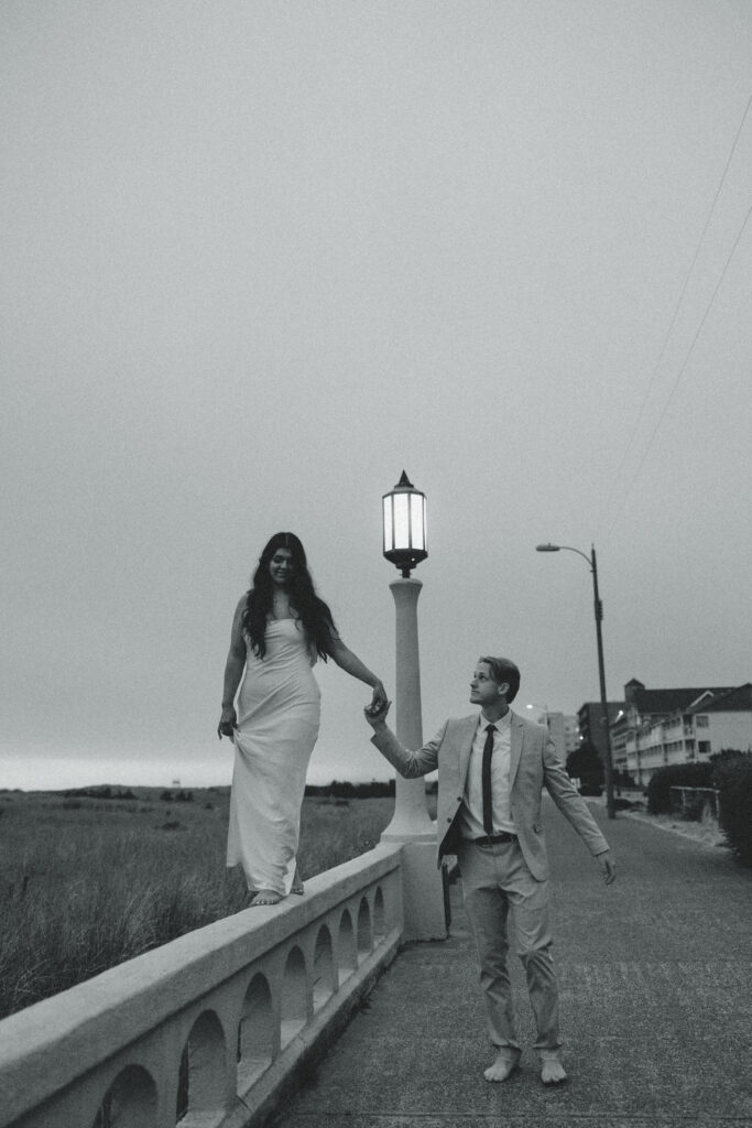 a woman walks along a railing as her husband holds her hand to steady her