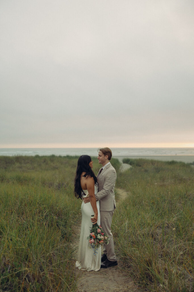 a couple looks at each other while standing in a path to the beach behind them during their elopement photography