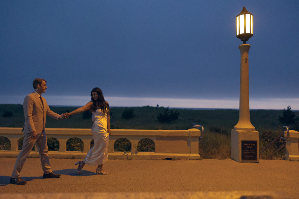 a la la land-esque photo of a couple walking for elopement photography, she walks in front and looks back at their entwined hands next to a lamppost