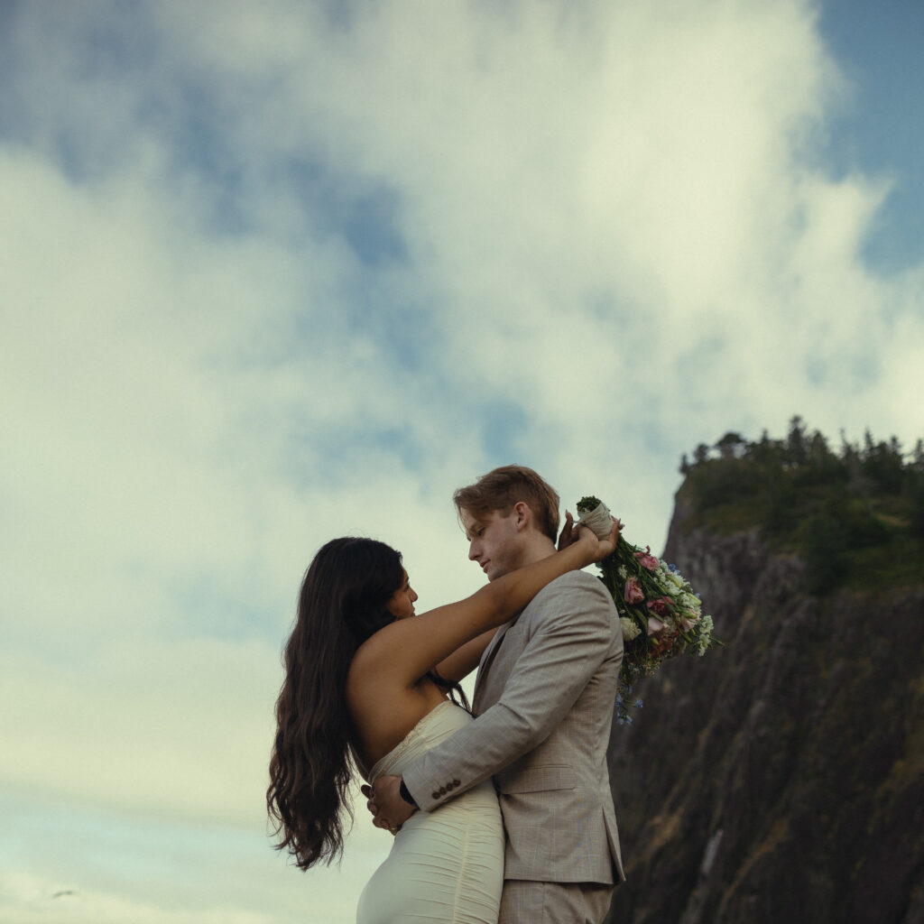 a couple stand in an embrace during elopement photography with the sky and a mountain behind them