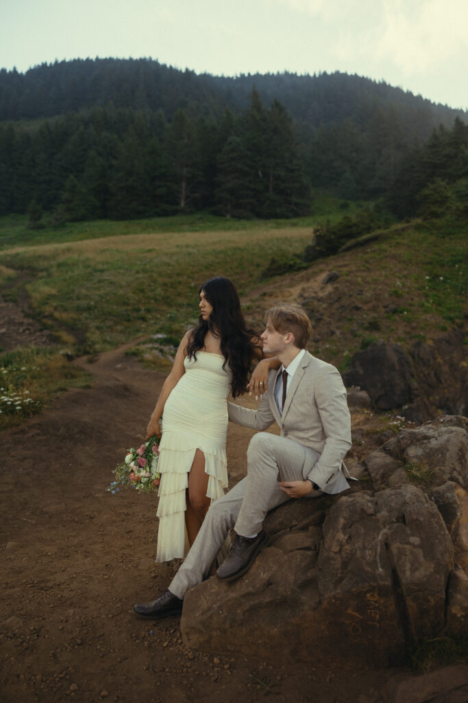 a couple eloping in oregon stand in wedding attire with a forest behind them