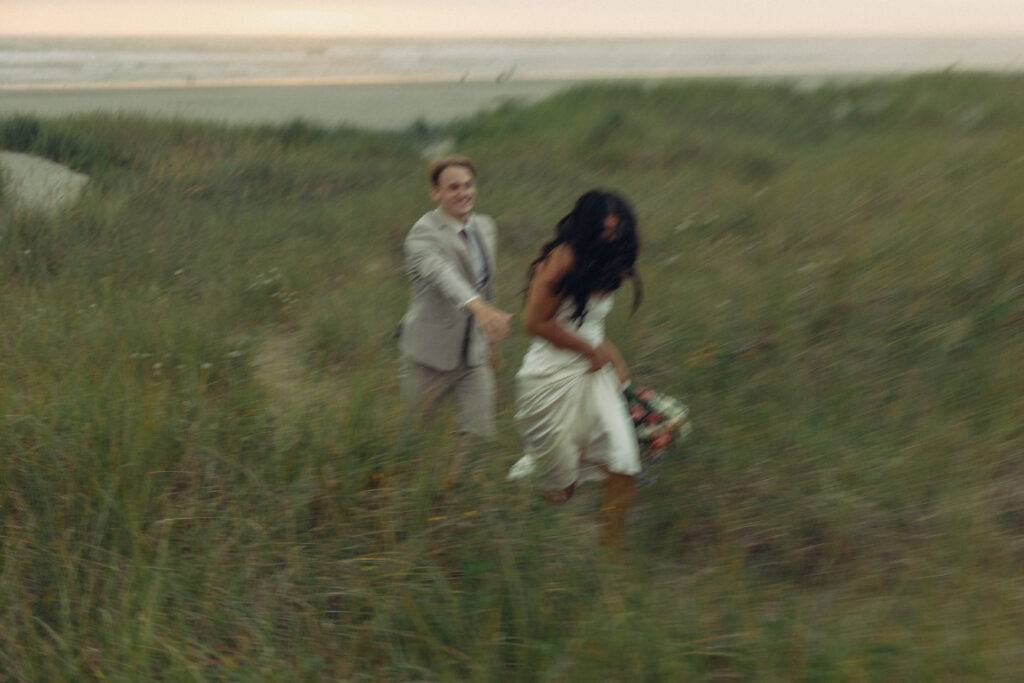 a couple frolics through a field in front of a beach during their oregon elopement