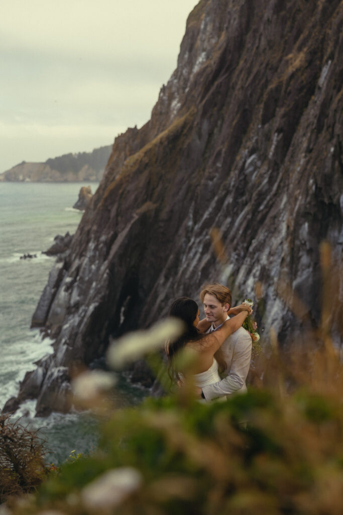 through the branches of a native plant, a couple dances with the ocean and a mountain behind them