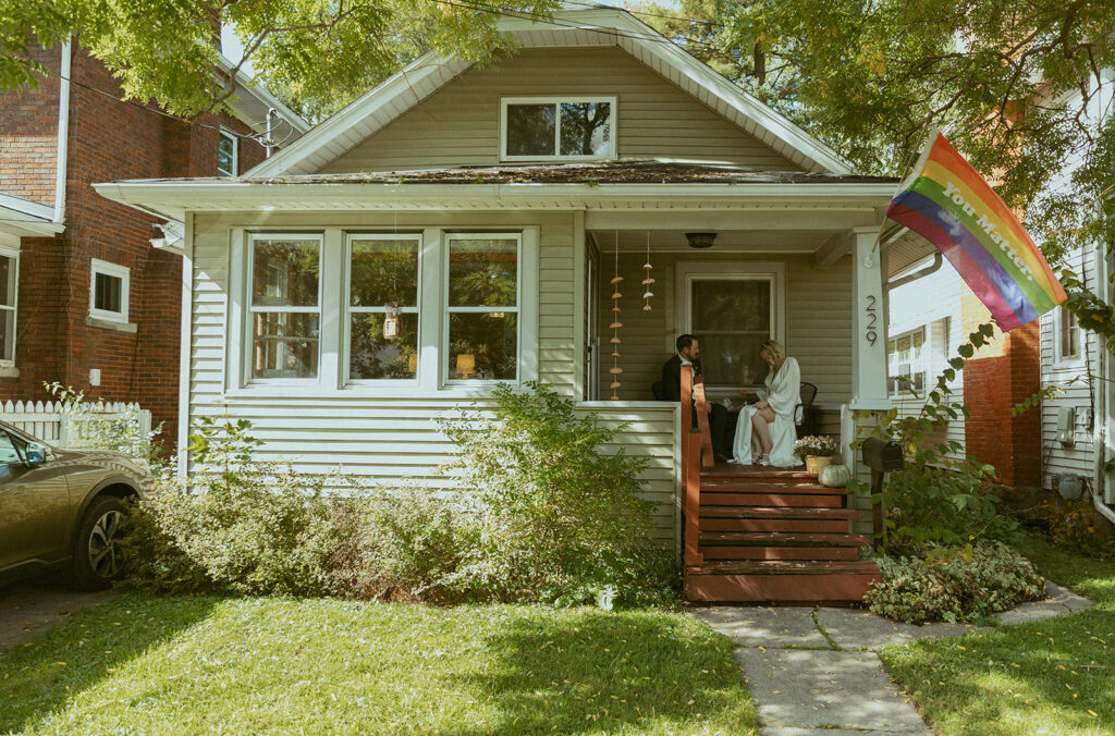 A newlywed couple is photographed following their MI elopement on the front porch of their home