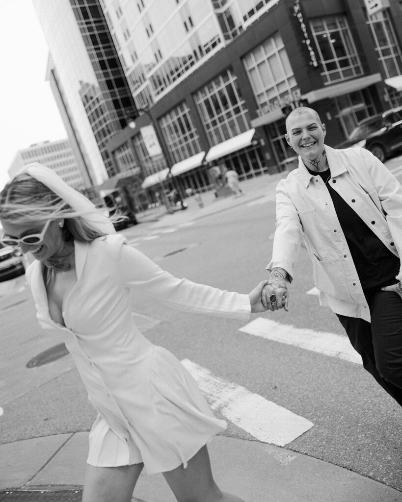 A newlywed couple holds hands as they cross the street downtown following their MI elopement ceremony