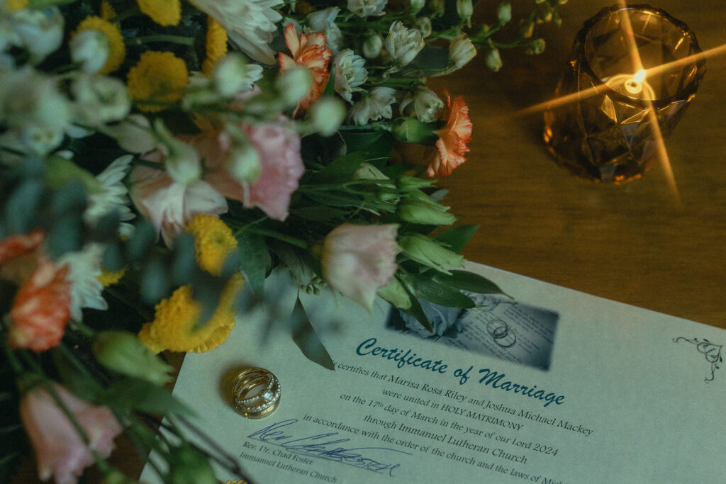 A detail shot from a Michigan elopement featuring wedding rings, the brides' bouquet, and the certificate of marriage 