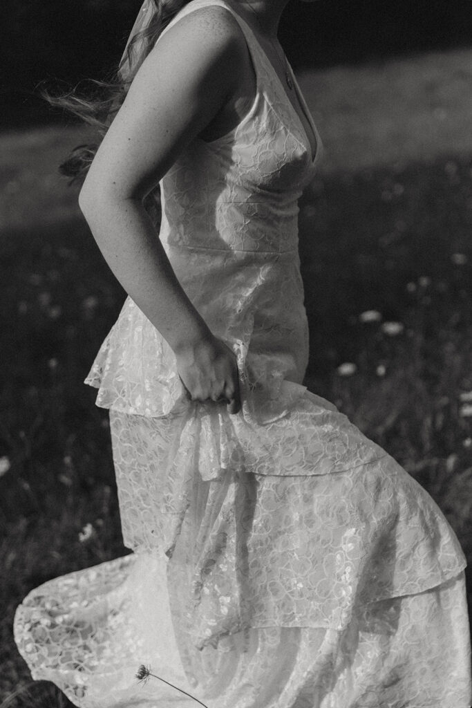 A black and white image of a Michigan bride in her wedding dress holding up the hem as she walks through a field following her elopement  