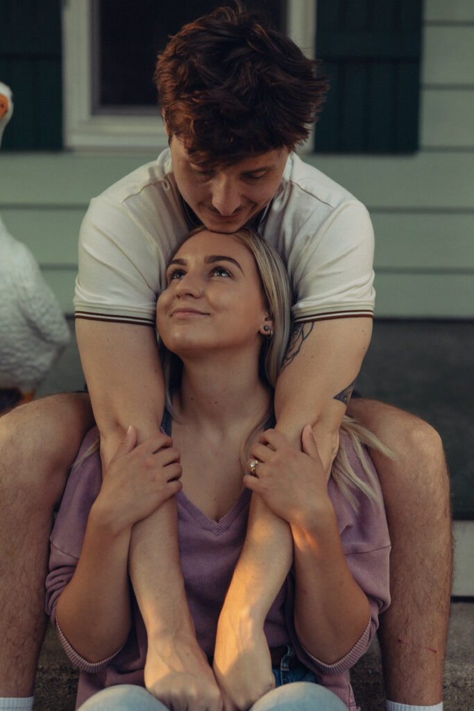 a man leans down with his arms on either side of his fiance's face as she smiles and holds his arms during engagement photos grand rapids