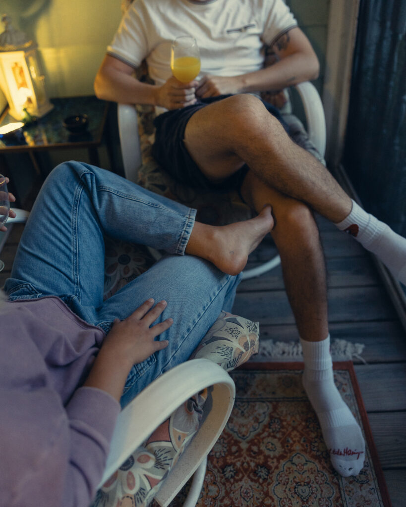 a cropped shot of an engaged couple having mimosas with their legs crossed on the porch during engagement photos