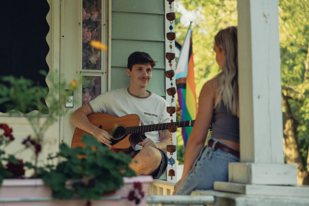 a man smiles at his fiance who sits across from him while holding a guitar