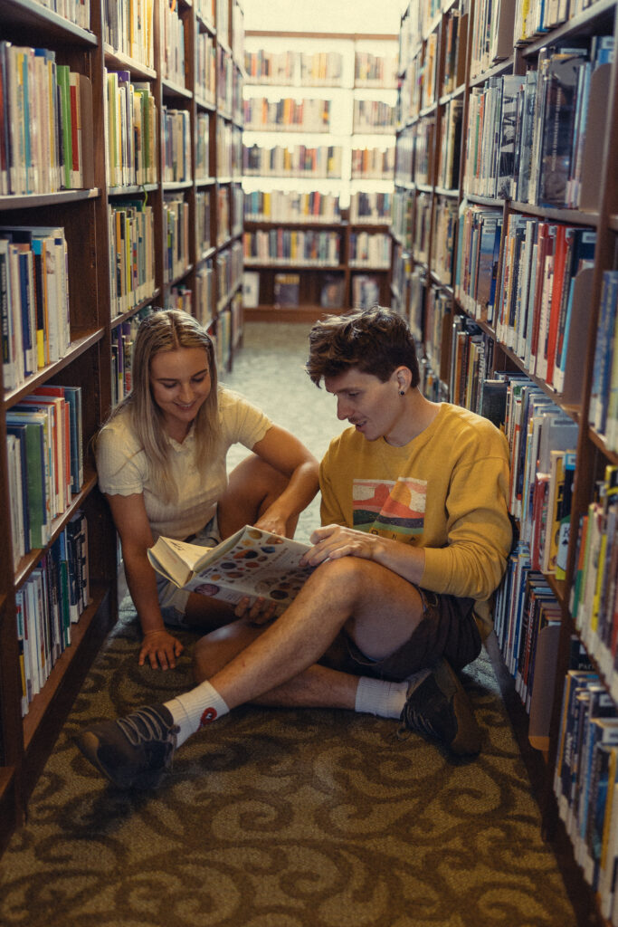 an engaged couple sits in between shelves of books at a library