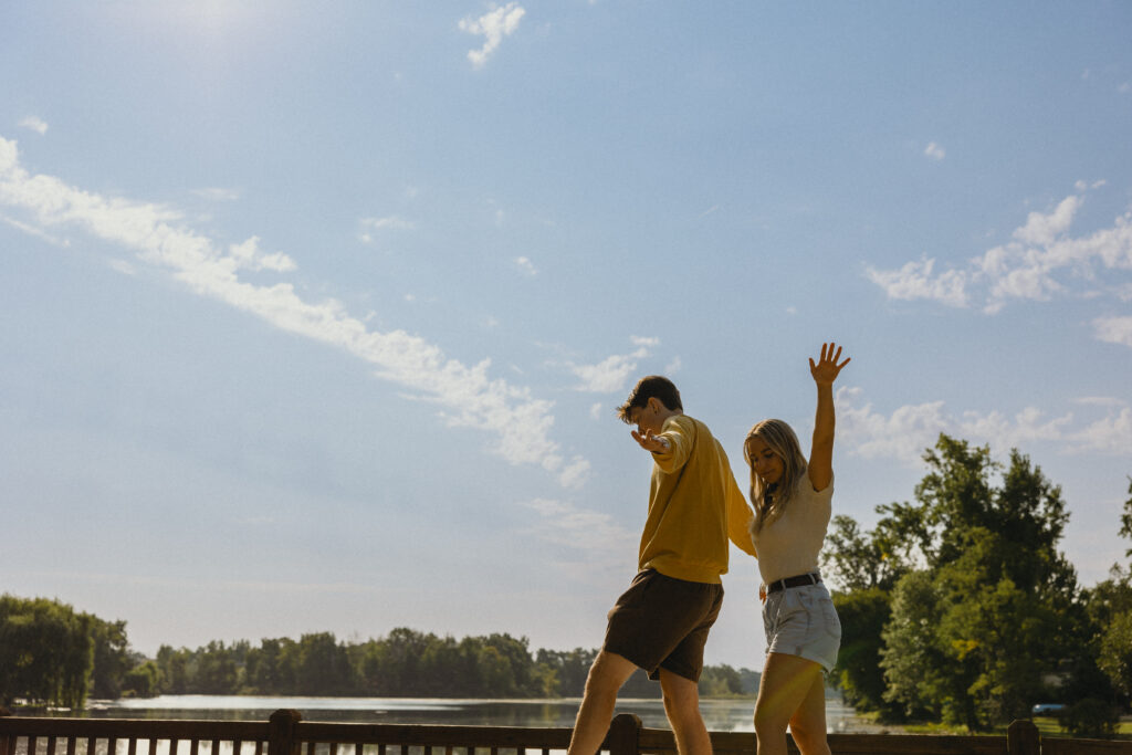 a couple walks with their arms out at their sides for balance on a sunny day for their engagement photos grand rapids