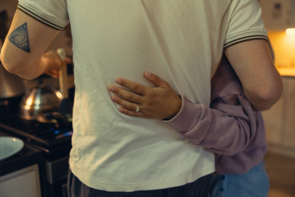 a woman rests her hand on her fiance's back showing off her engagement ring during engagement photos