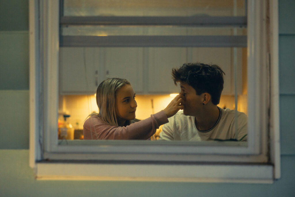 a woman wipes her fiance's face as they sit framed in the window during engagement photos grand rapids