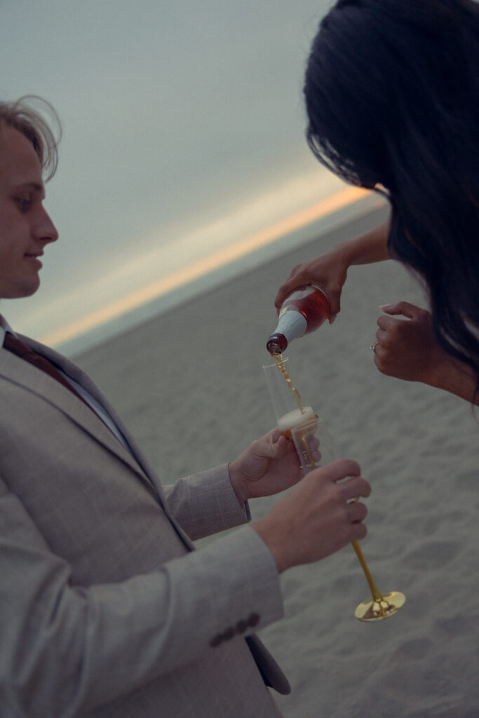 a woman pours champagne into a glass that her husband holds during elopement photography for their oregon elopement