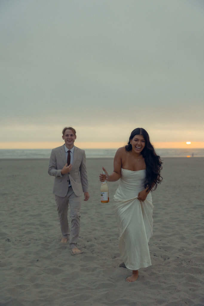 a couple laughs together on the beach after they pop champagne during their elopement photography