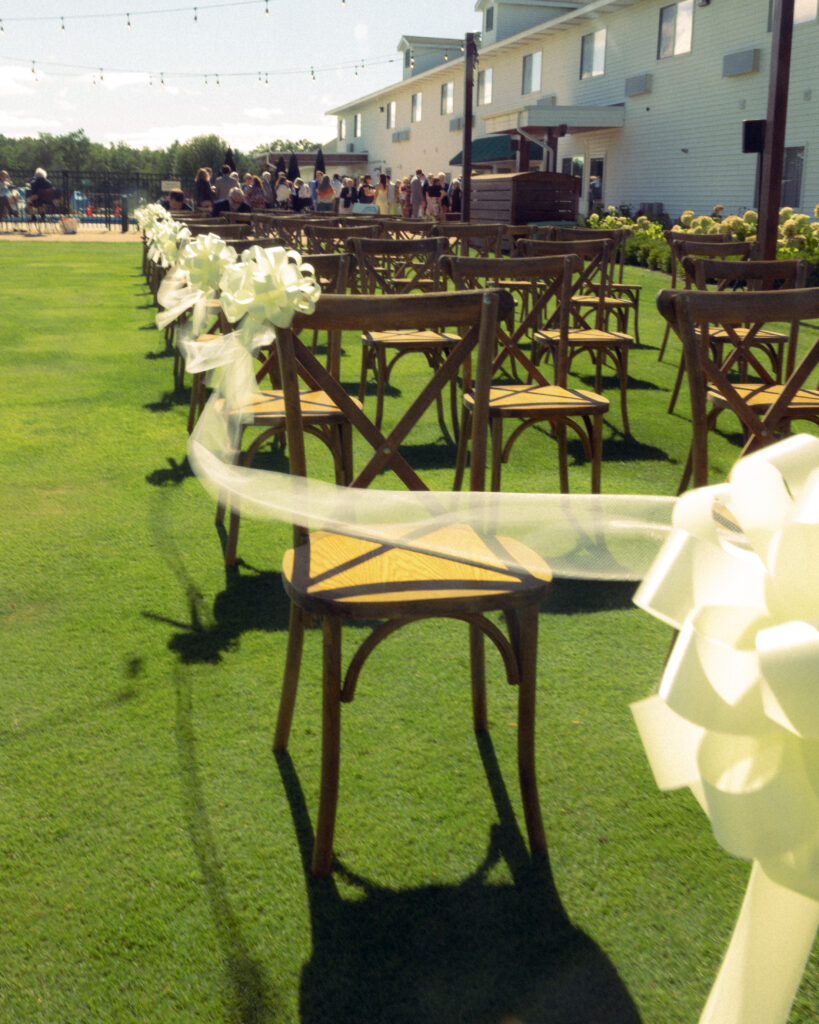 wedding guests stand in a crowd in the distance with chairs in rows in the foreground