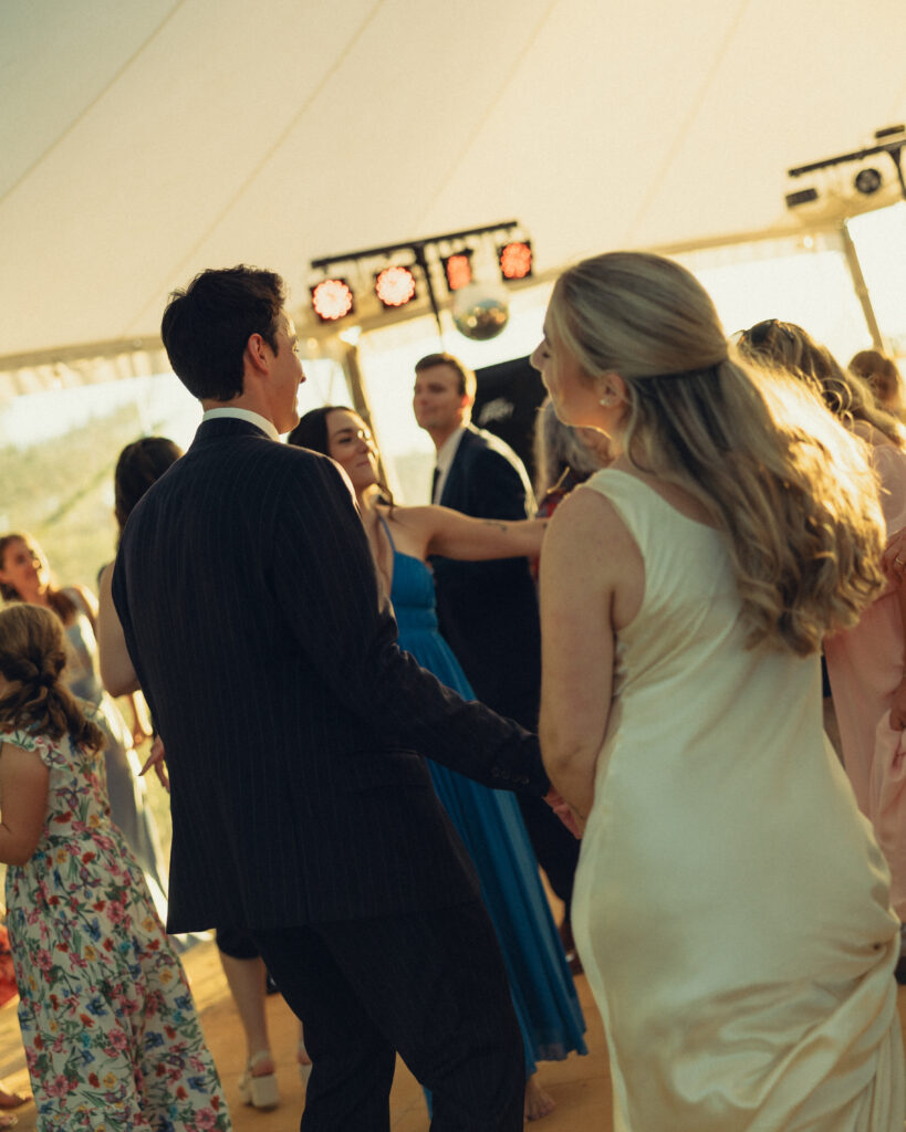 documentary style wedding photos, the bride and groom dance together with their guests on the dance floor enjoying the moment