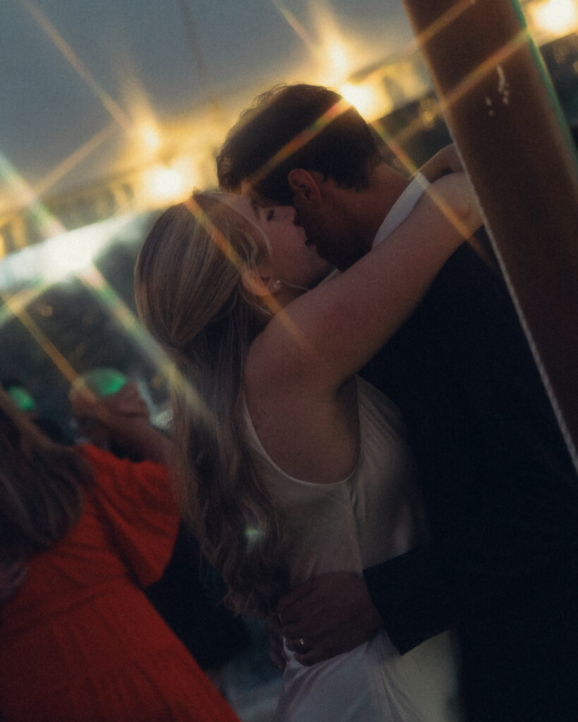 the bride leans in to whisper to the groom while they lean together on the dance floor with lights sparkling behind them during their reception with documentary style wedding photos