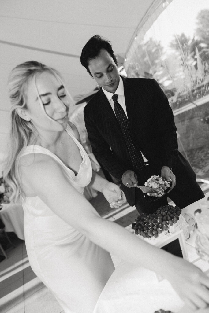 the bride reaches for a plate as she and the groom cut the cake at their reception with documentary style wedding photos