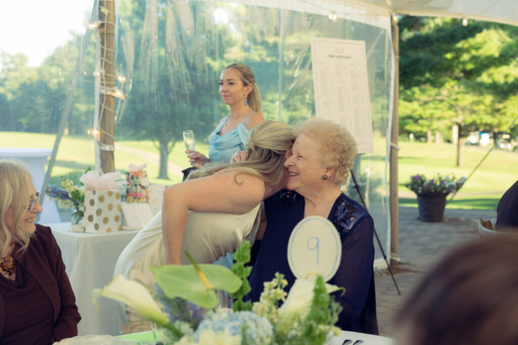 the bride shares and embrace with a smiling guest at table nine in documentary style wedding photos