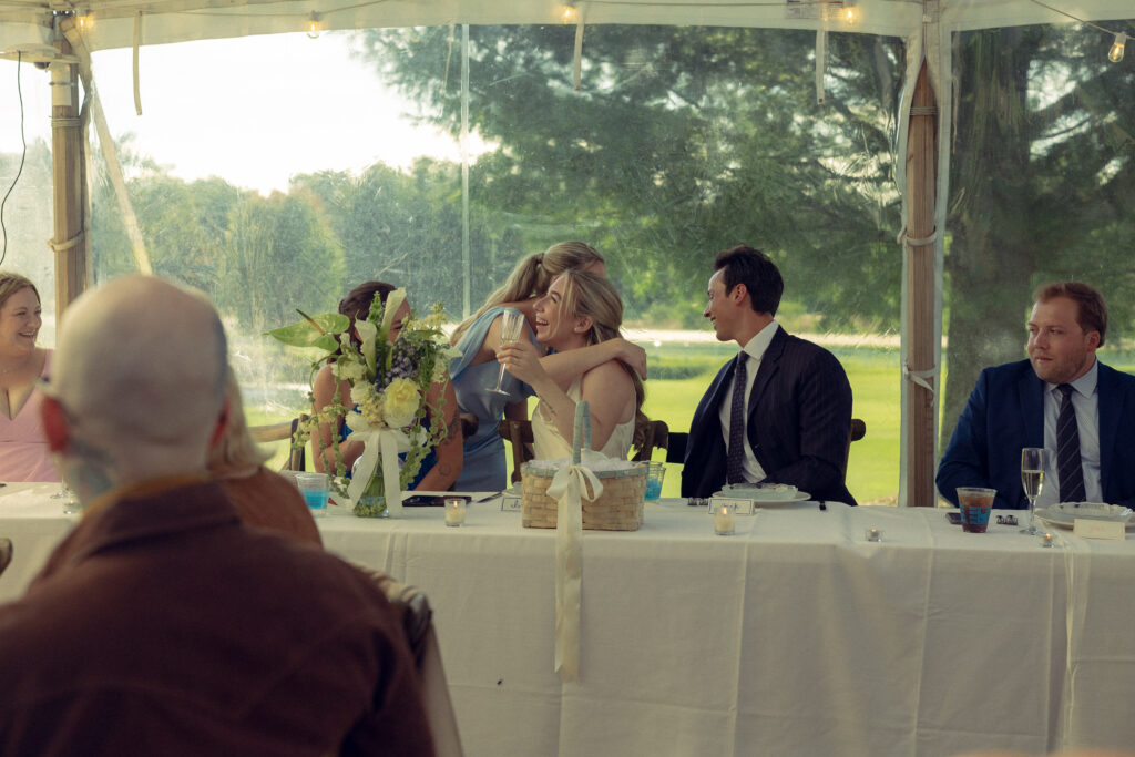 the bride shares a hug with the bridesmaid as everyone smiles in documentary style wedding photos