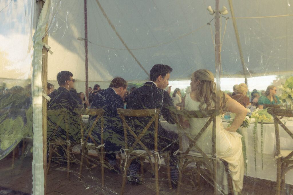 a photo of the bride and groom eating through the clear wedding tent for documentary wedding photos