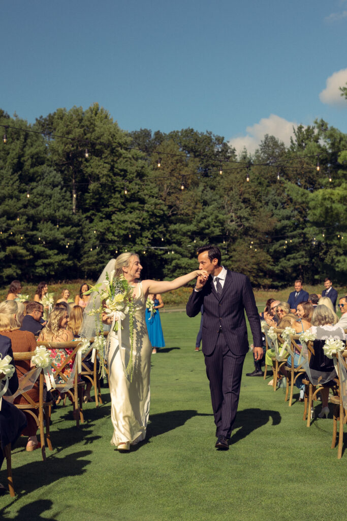 the bride holds her arm out as her new husband presses a kiss to it as they walk down the aisle during documentary style wedding photos