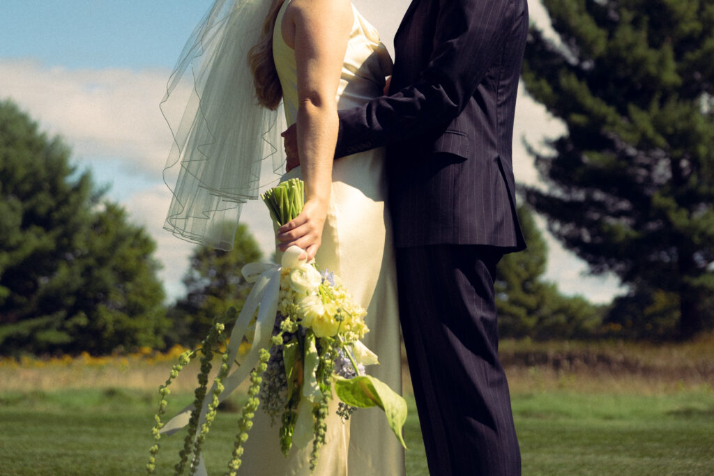 the bride and groom stand in an embrace outside on a sunny day