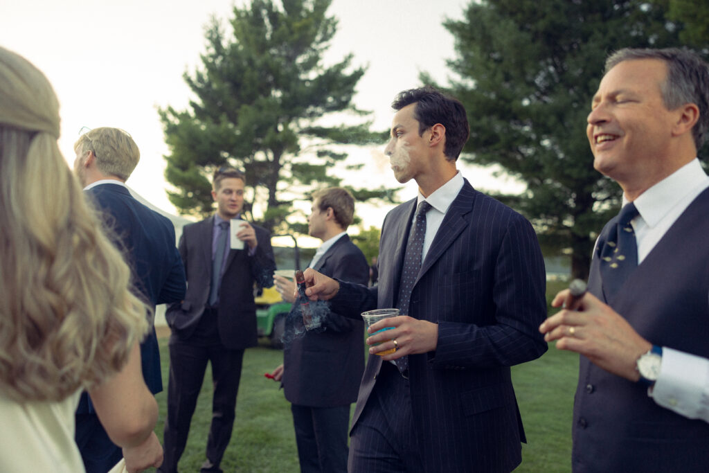 the groom blows cigar smoke outside during the wedding reception with documentary style wedding photos