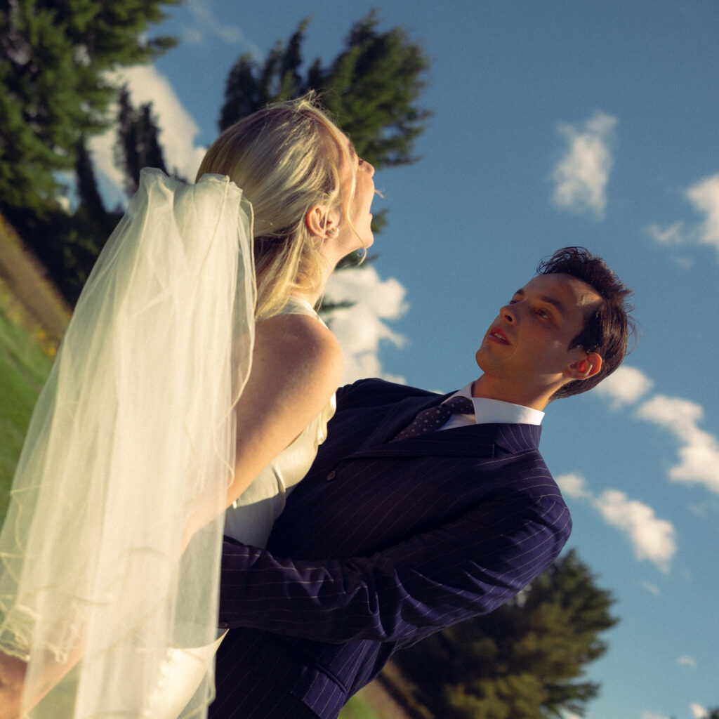 the bride looks up at the sky with a joyous face while her husband stares at her