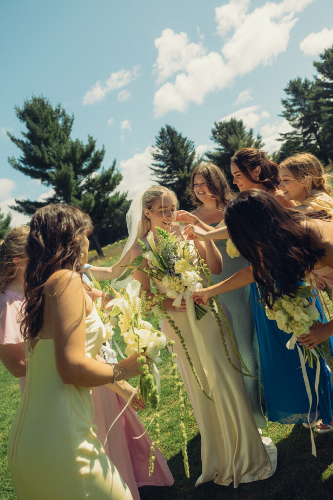 a bride smiles as her bridesmaids all touch her in this documentary style wedding photo