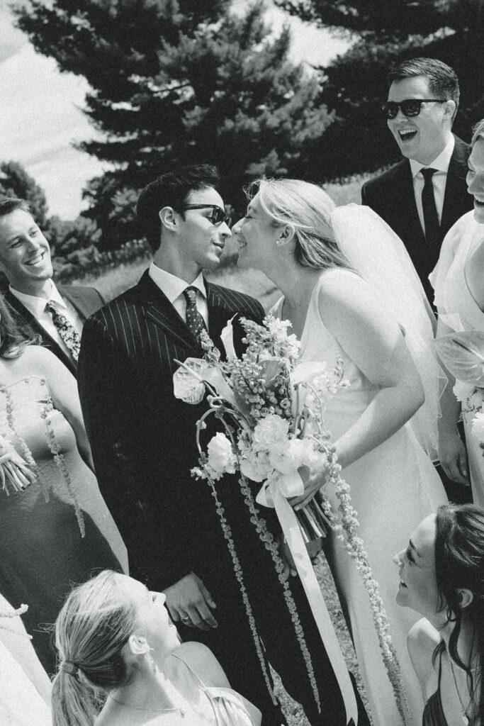 the bride and groom lean into a kiss with their wedding party standing around them