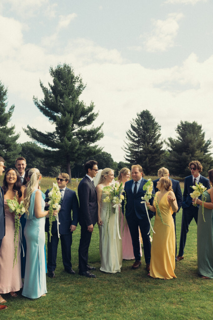 the entire bridal party stands in a field, each person looking in different directions in this documentary style wedding picture