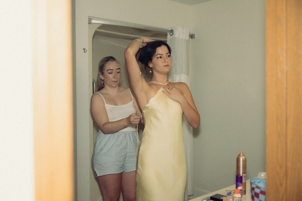 the bride helps a bridesmaid into her dress in this documentary style wedding photo